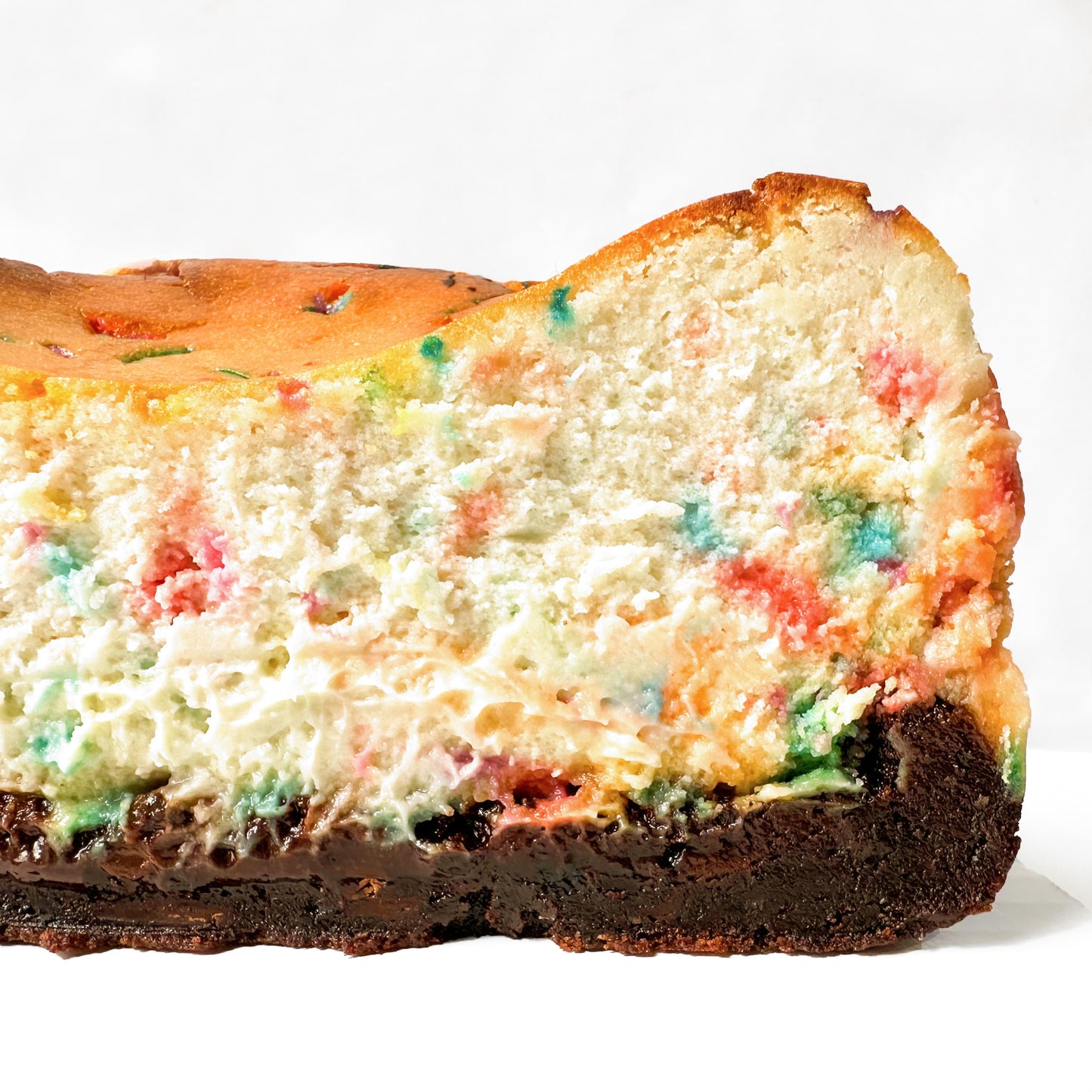 Birthday sprinkle cheesecake sliced in half, with a gooey chocolate brownie base.