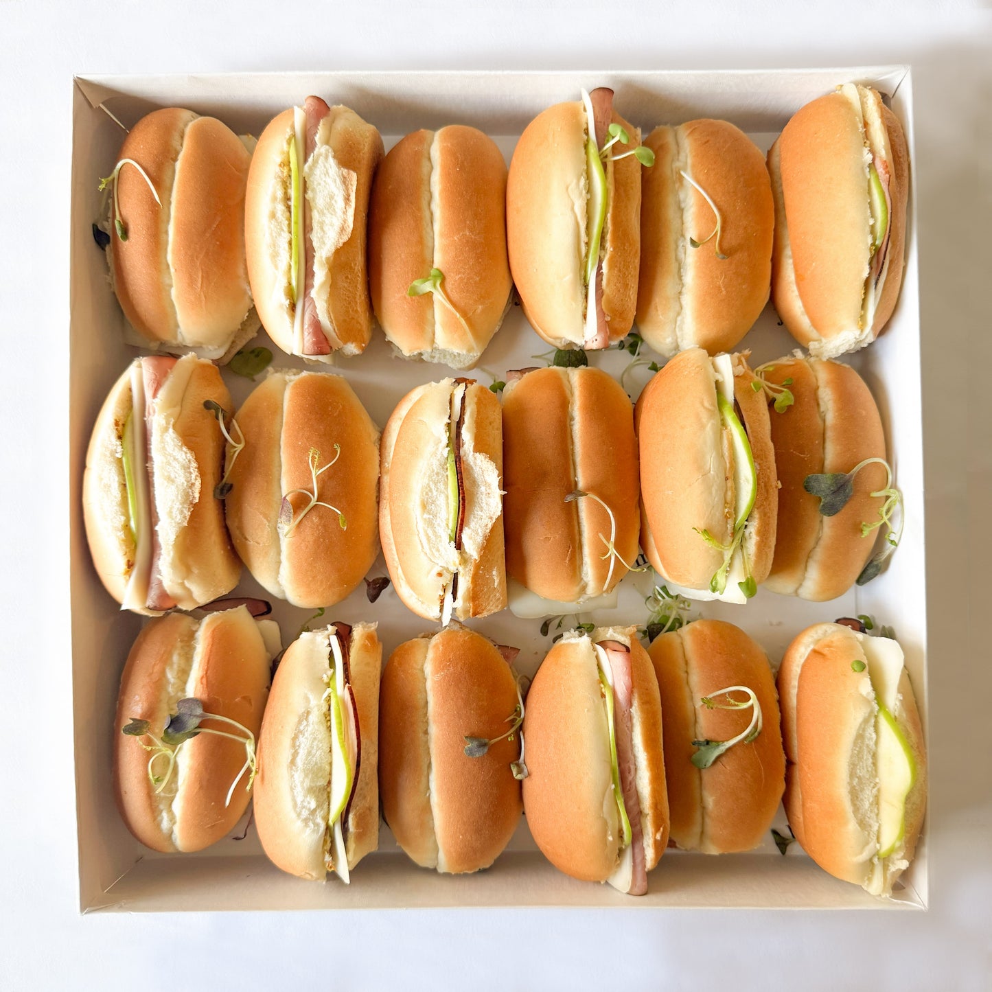 Box of mini dinner roll sandwiches with ham, cheese and sliced apples on a white background