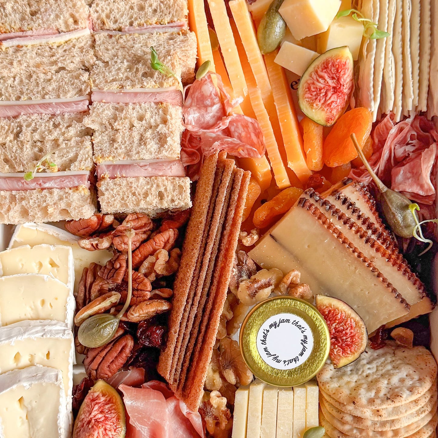 Assorted charcuterie board with meats, cheeses, mini tea sandwiches, fresh fruit, and crackers in a box, perfect for gifting.