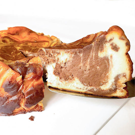 A slice of burnt basque cheesecake showing swirls of chocolate and vanilla interior on a white table.