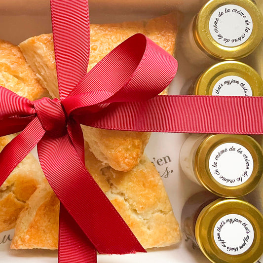Gift box with scones and jars of jam and clotted cream tied with a red ribbon.