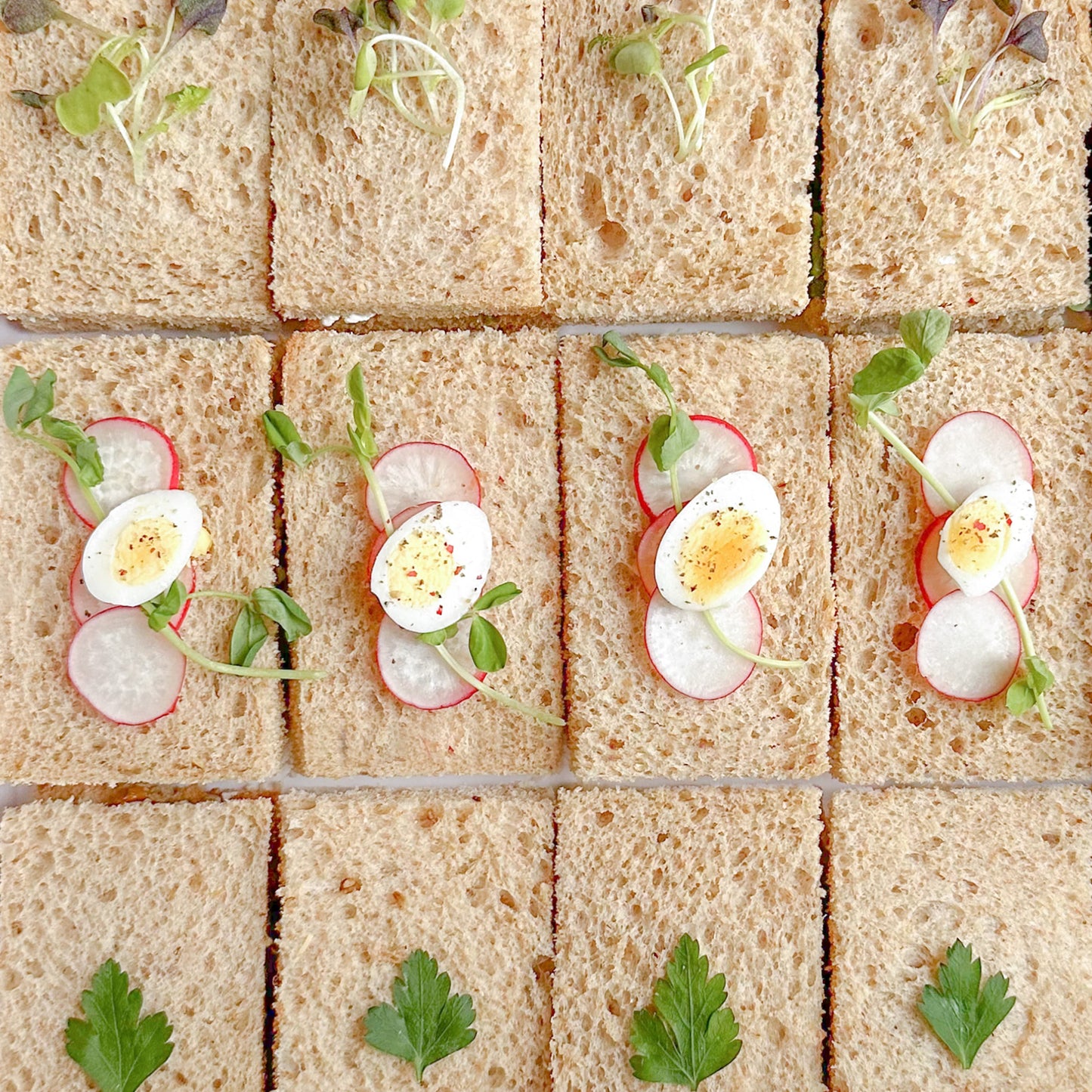 Assorted tea sandwiches decorated with herbs, microgreens and quail eggs.