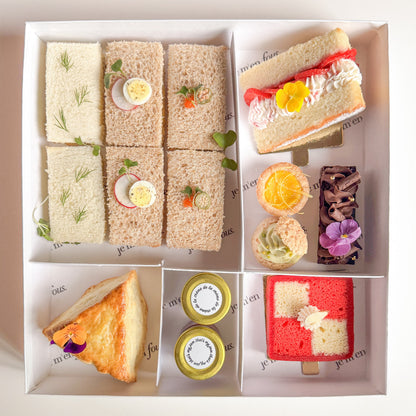 A boxed tea box with 6 assorted finger sandwiches, triangle scone with jam and clotted cream, mini desserts and cherry battenberg cake.