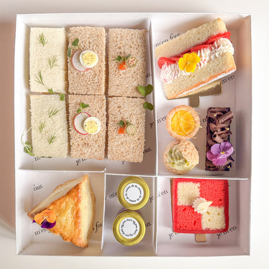 A boxed tea box with 6 assorted finger sandwiches, triangle scone with jam and clotted cream, mini desserts and cherry battenberg cake.