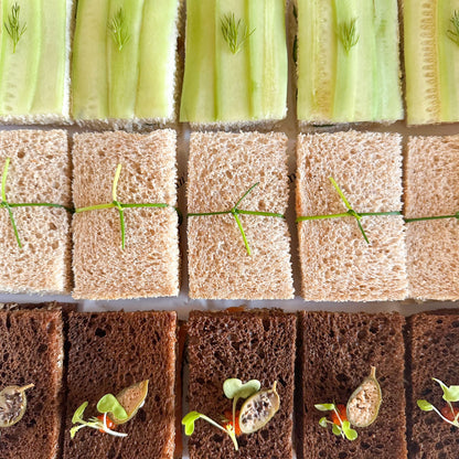 A box of assorted tea sandwiches with various fillings, such as cucumber, egg salad and smoked salmon, neatly arranged in rows in a white box.