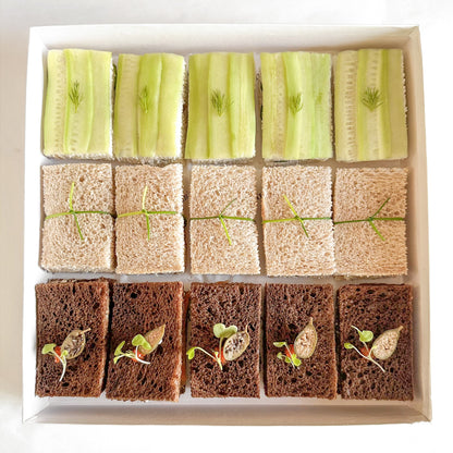A box of assorted tea sandwiches with various fillings, such as cucumber, egg salad and smoked salmon neatly arranged in rows and served in a white box.