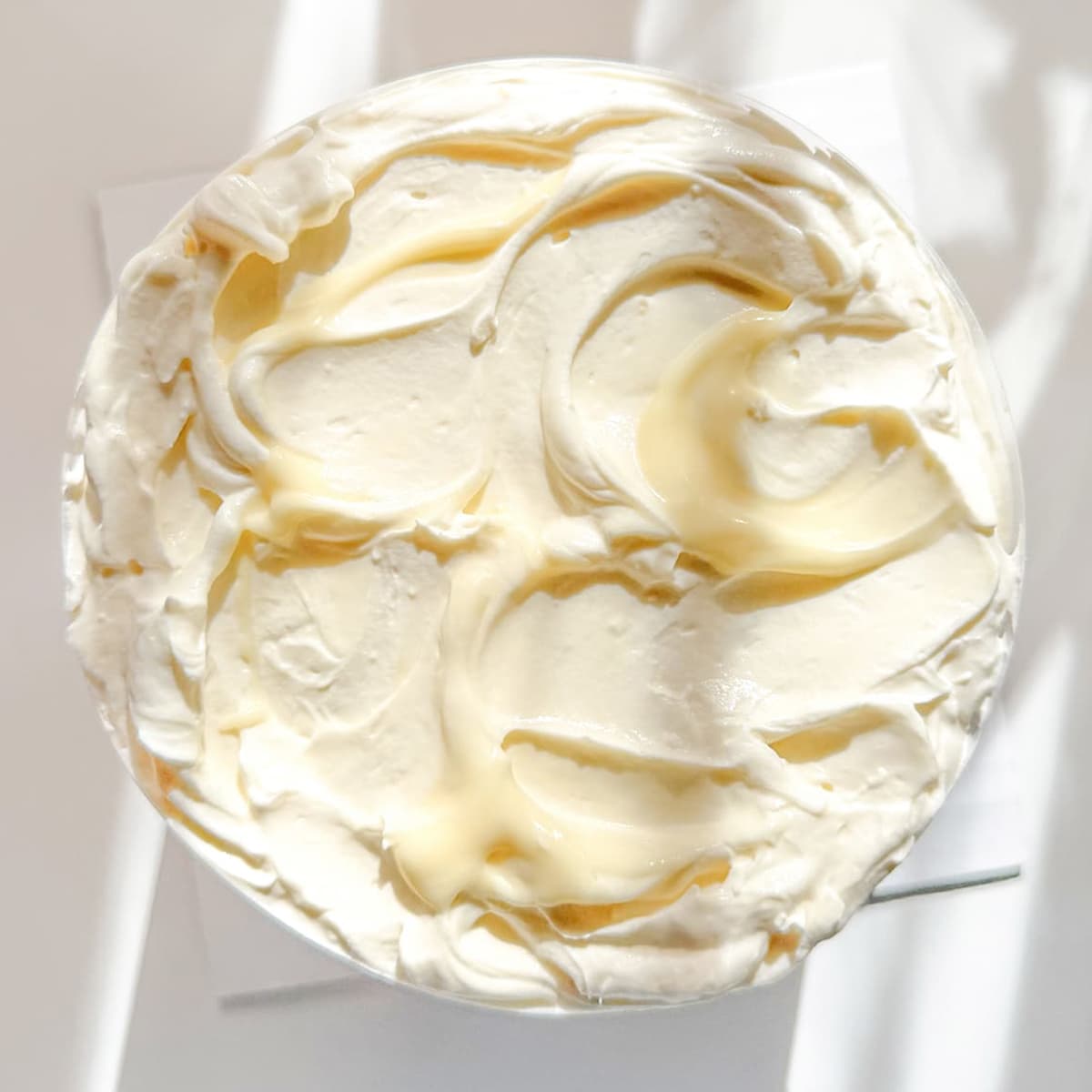 A top-down view of a round white whipped cream and banana pudding swirled together, on a white surface with soft shadow.