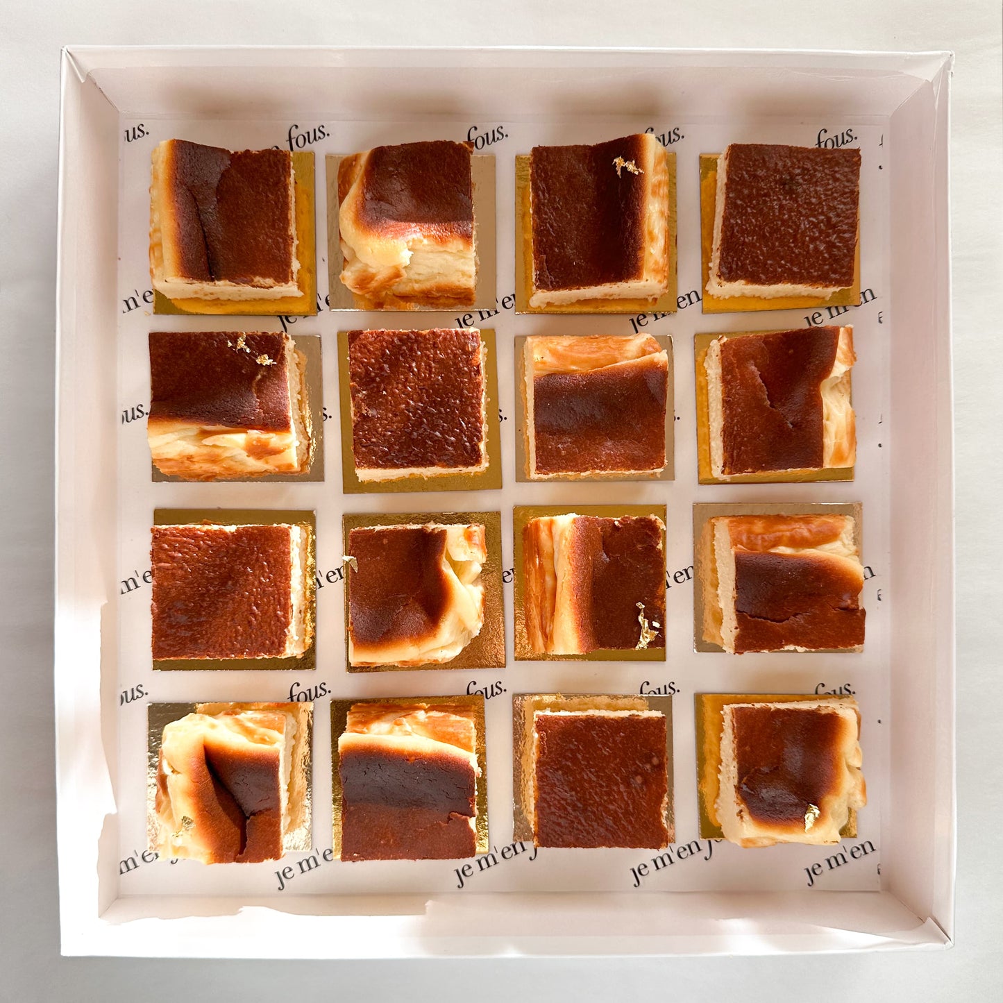 White box with mini burnt basque cheesecake squares on gold boards, ready to serve.