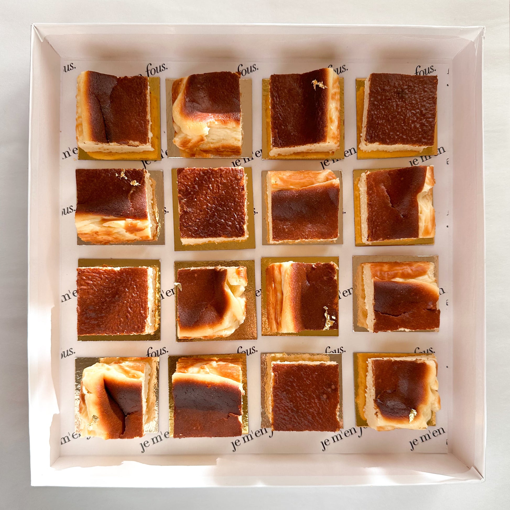 White box with mini burnt basque cheesecake squares on gold boards, ready to serve.