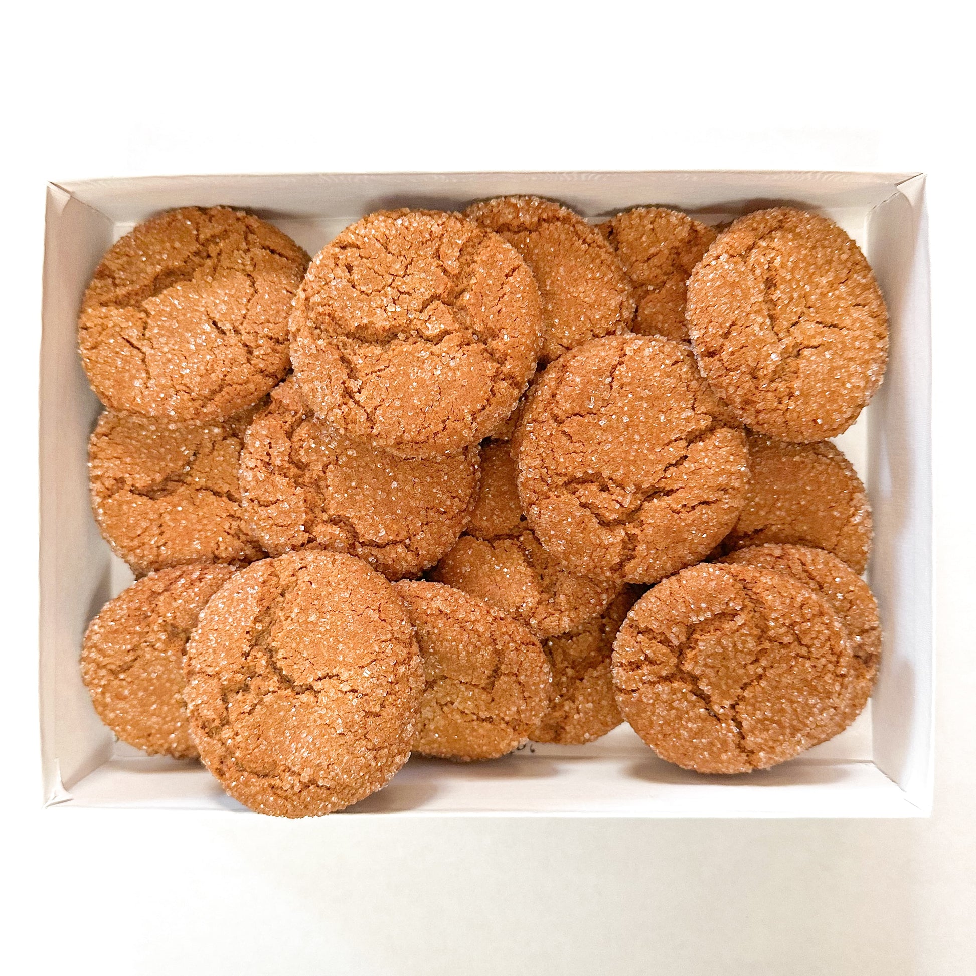 Box filled with chewy gingerbread cookies rolled in sugar on a white background.