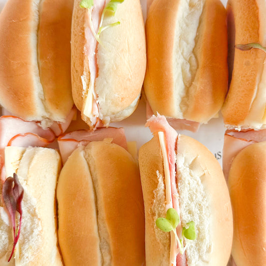 Box of mini dinner roll sandwiches with ham and cheese on a white background