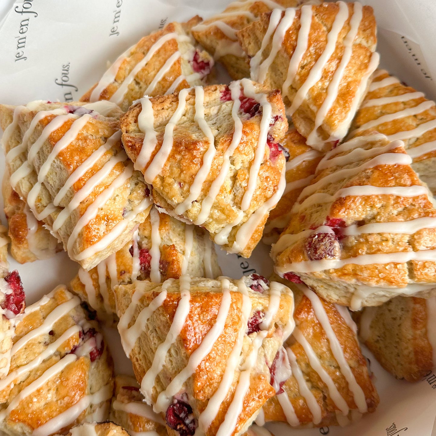 Box filled with triangle shaped orange cranberry scones with a vanilla drizzle.