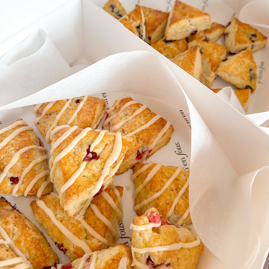 White boxes with mini triangle shaped scones, including orange cranberry and blueberry.