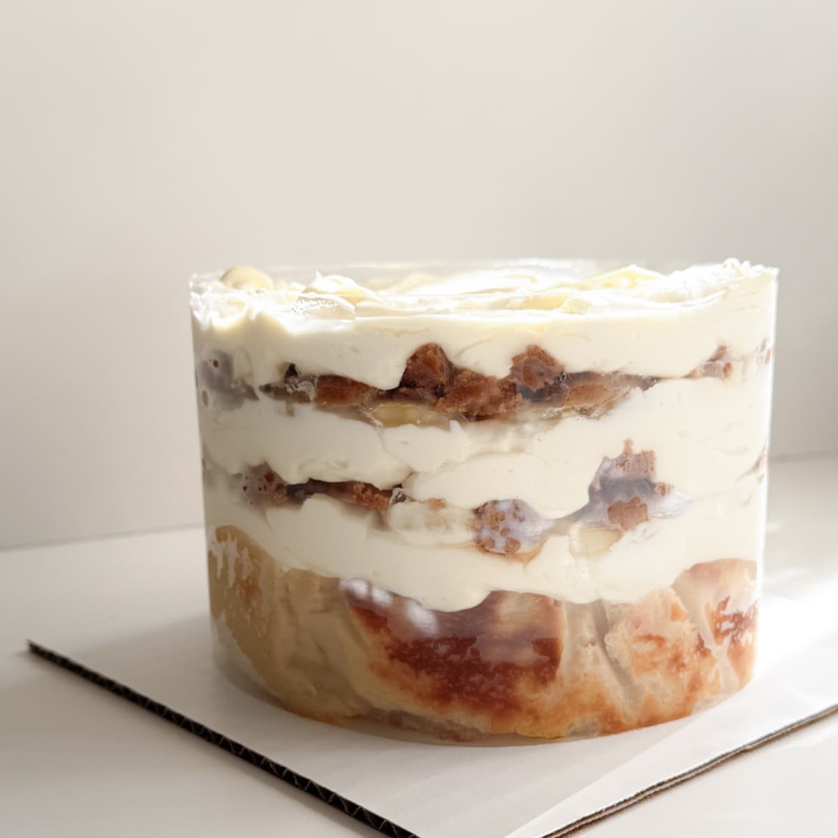 A layered banana pudding cake, with white whipped cream, biscoff cookies, and sliced bananas, photographed on a white surface against a light neutral background.