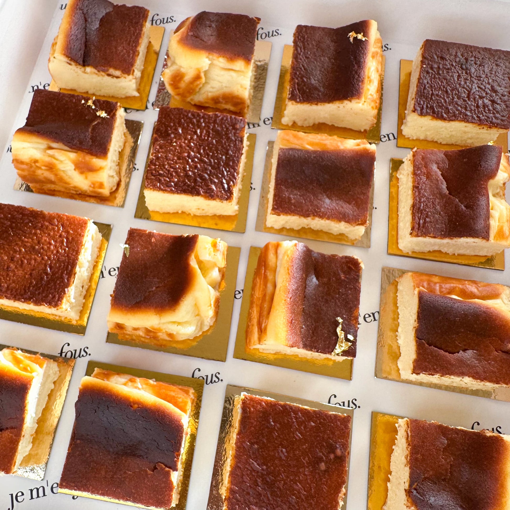 Mini burnt basque cheesecake squares decorated with gold leaf, ready to serve on gold boards.