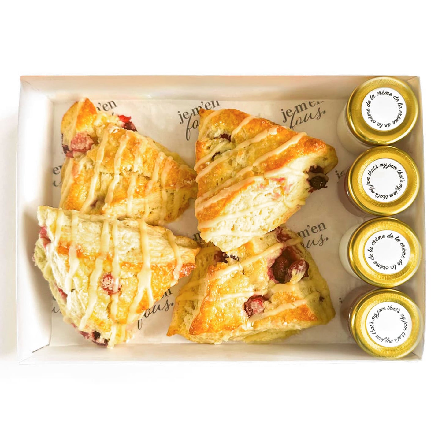 Box of triangle orange cranberry scones with jars of jam and clotted cream on a white background.