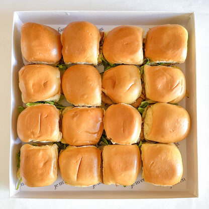 A box of prepared roast beef brioche sandwiches with caramelized onions and arugula in a white box.