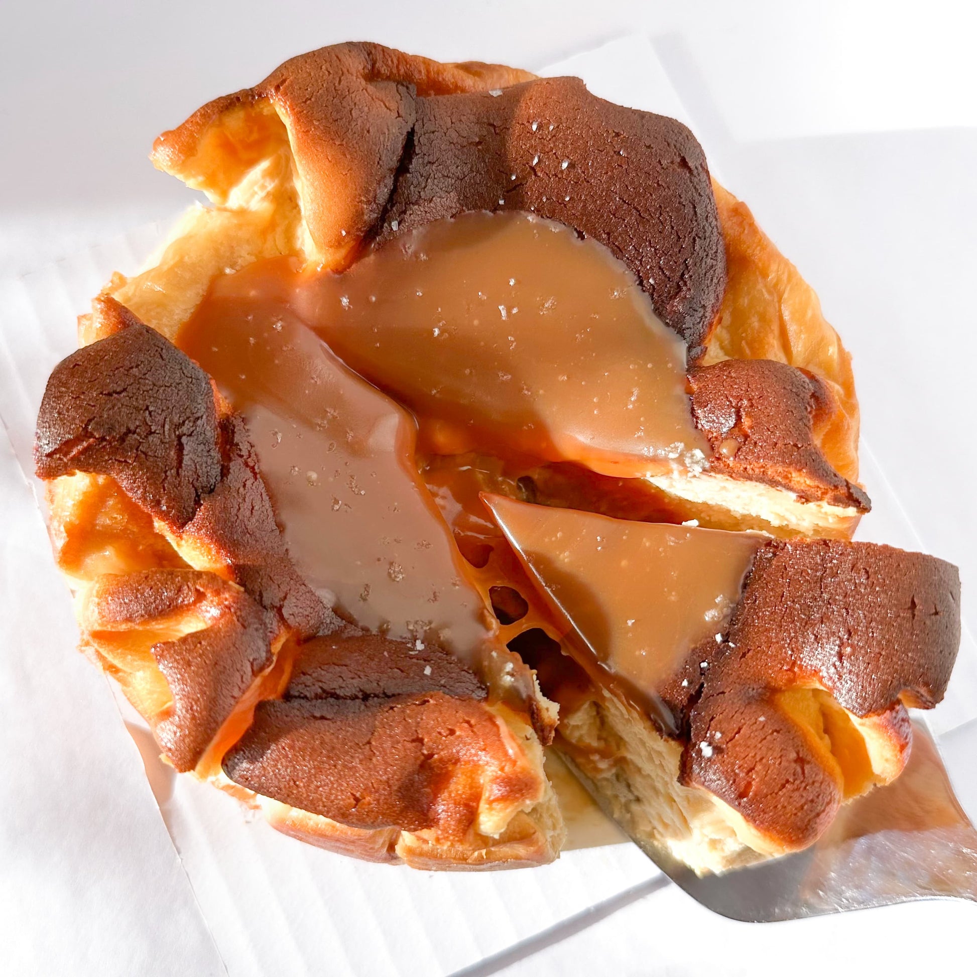 Caramel burnt basque cheesecake with slice being served on a white table.