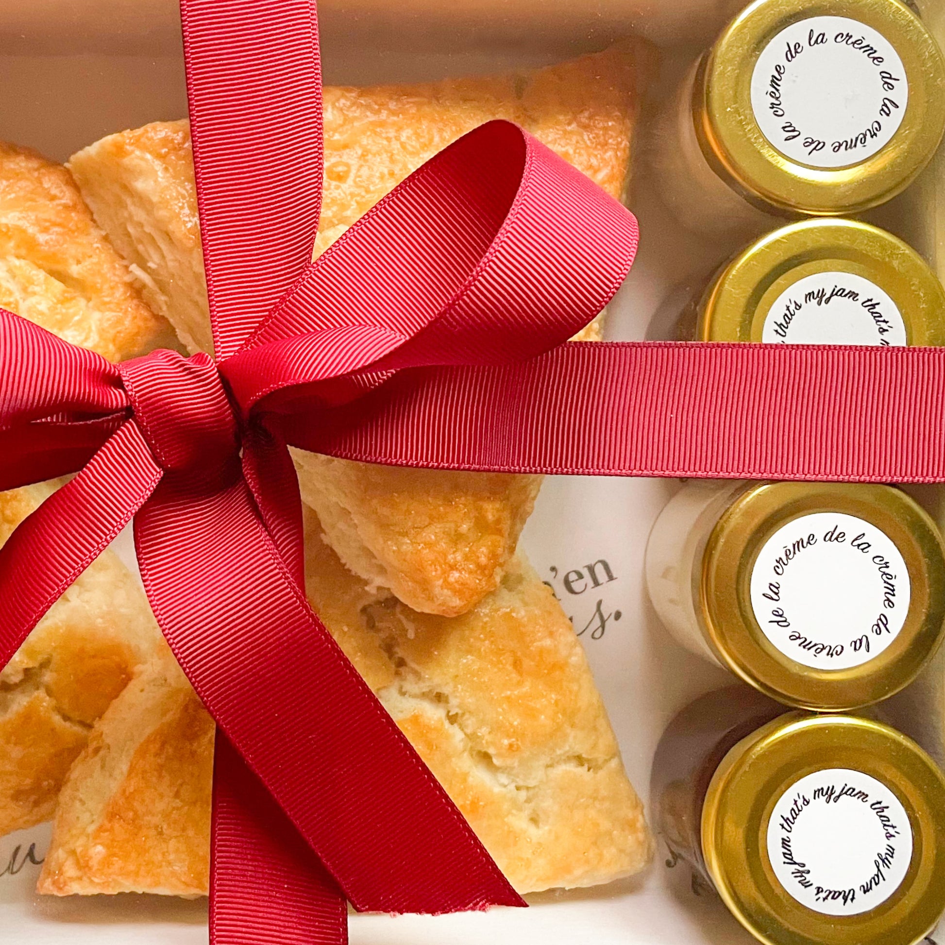 Gift box with scones and jars of jam and clotted cream tied with a red ribbon.