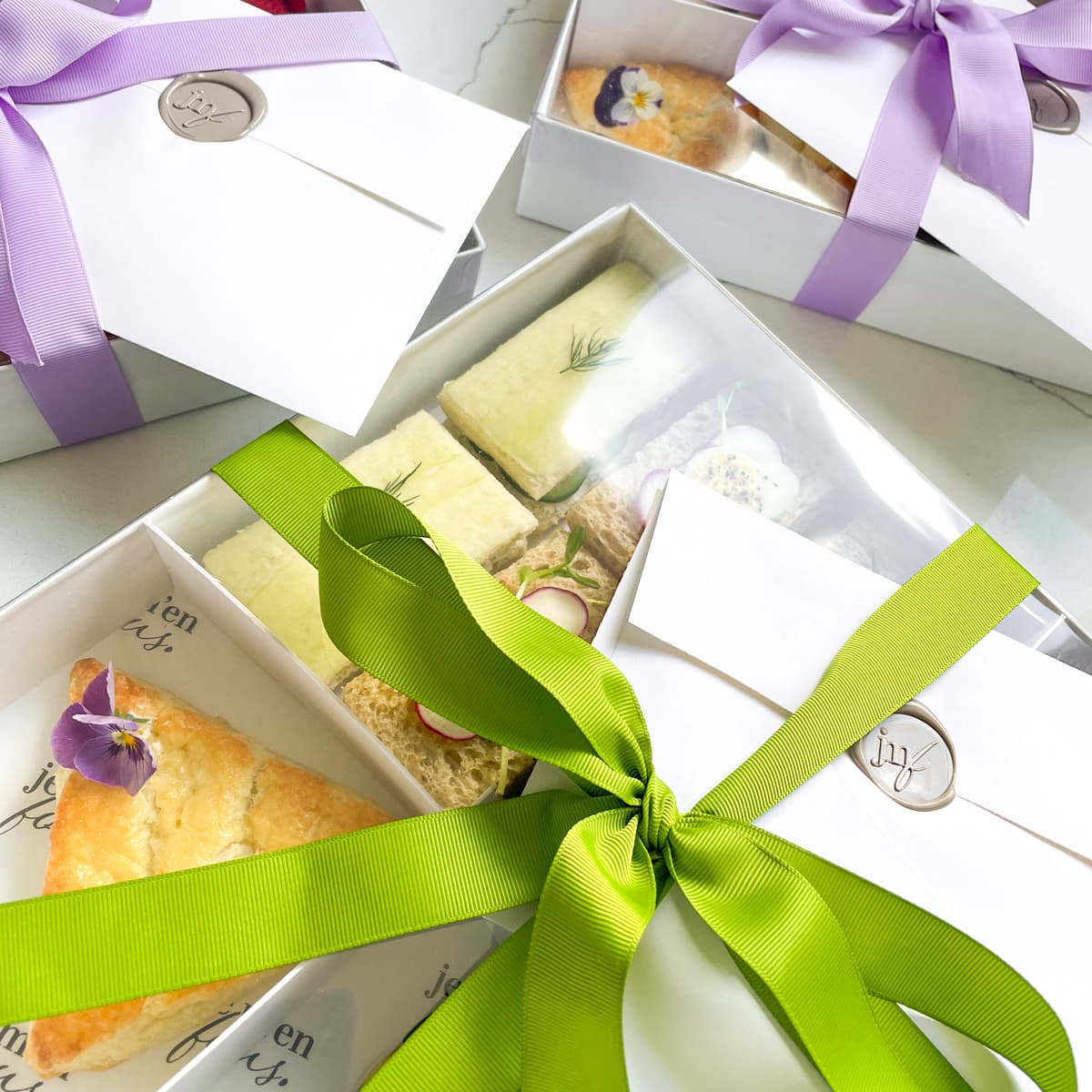 Afternoon tea boxes wrapped in purple and green ribbon and wax sealed envelopes.
