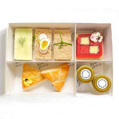 Box filled with assorted tea sandwiches, mini triangle scones, jam and clotted cream and mini cherry vanilla battenberg cake.