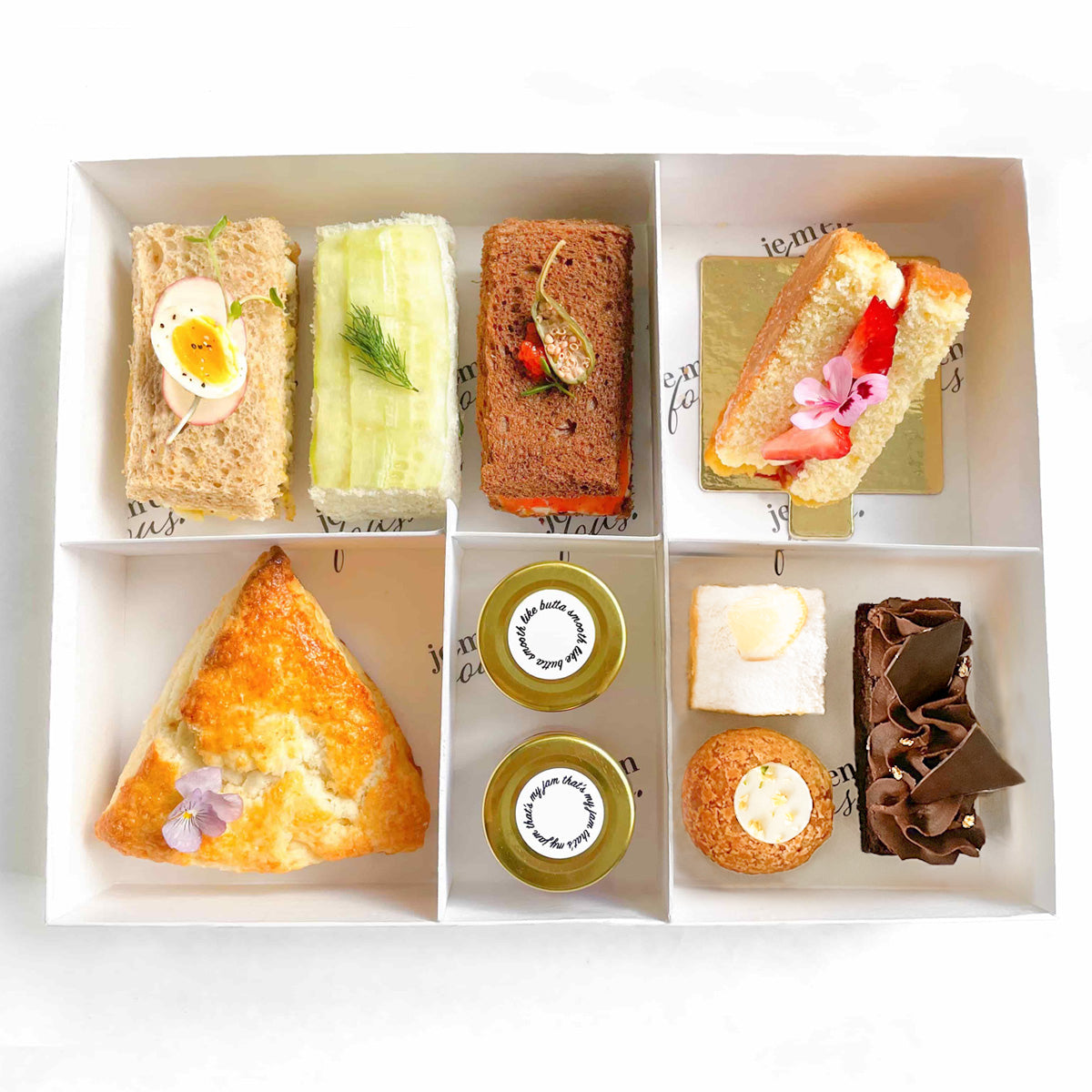 A tea box containing an assortment of finger tee sandwiches, a triangle scone with jam and clotted cream, and mini desserts.