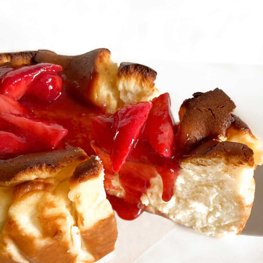 Burnt basque cheesecake slice being served with strawberry on top, on a white table.